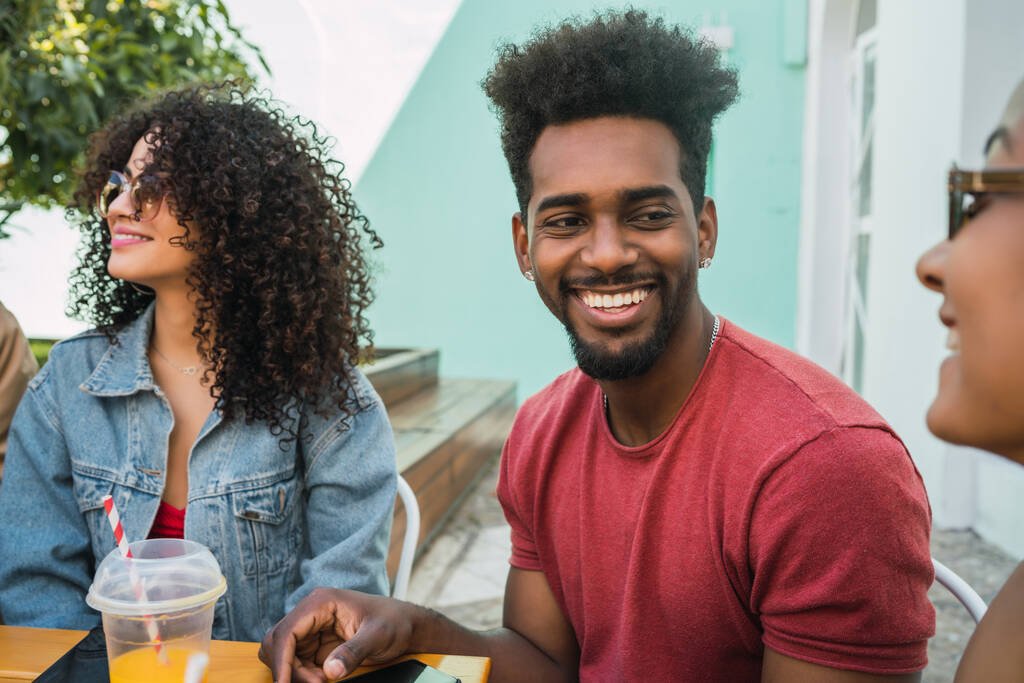 Retrato de amigos afro divirtiéndose juntos y disfrutando de un buen rato mientras beben jugo de fruta fresca al aire libre en la cafetería
. - Foto, imagen