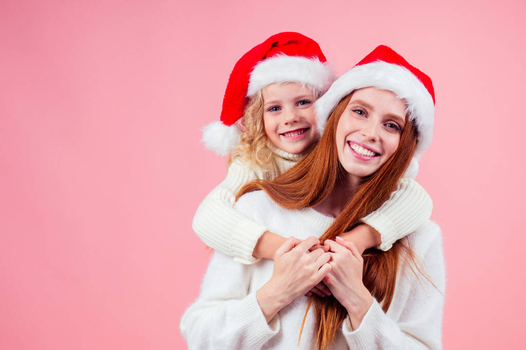 ,щаслива руда імбирна жінка і мила маленька блондинка в капелюсі Санта Клауса і розважається разом у студійному рожевому фоні
 - Фото, зображення