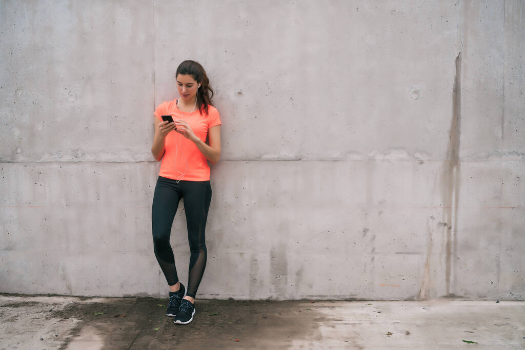 Retrato de una mujer atlética usando su teléfono móvil en un descanso del entrenamiento. Deporte y salud estilo de vida. - Foto, imagen
