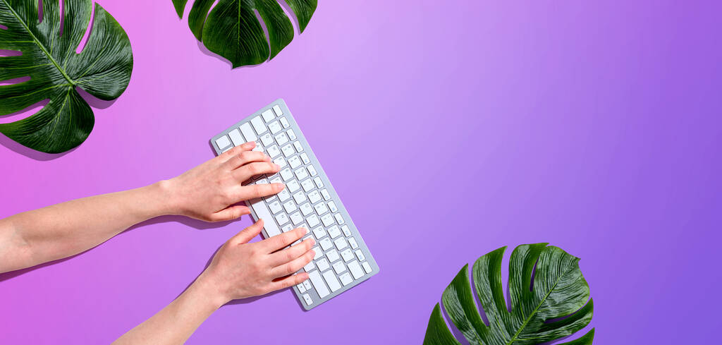 Person using a computer keyboard with tropical leaves - Photo, Image