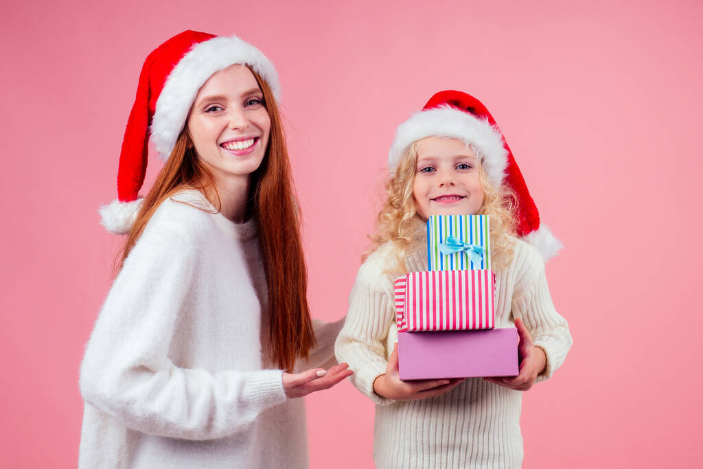 отримання різдвяних подарунків.дівчата в червоному капелюсі Санта тримають купу подарункових коробок на рожевому фоні студії
 - Фото, зображення