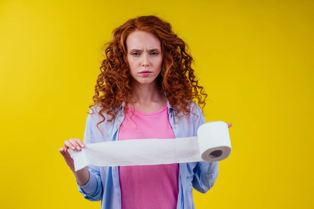 Beautiful curly redhead ginger woman holding toilet paper roll on yellow color background - Photo, Image