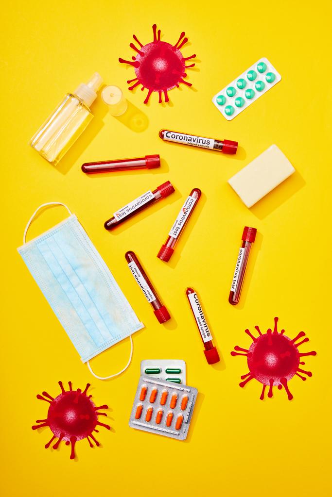 górny widok probówek z napisem koronawirusa w pobliżu maski medycznej, blistry z tabletkami, butelka z środkiem do dezynfekcji rąk i pasek mydła na żółto  - Zdjęcie, obraz