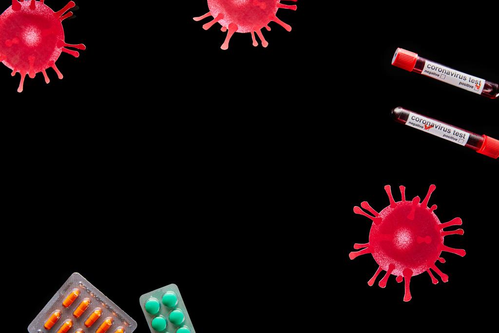 bovenaanzicht van blisterverpakkingen met pillen en reageerbuisjes met coronavirus testletters geïsoleerd op zwart  - Foto, afbeelding