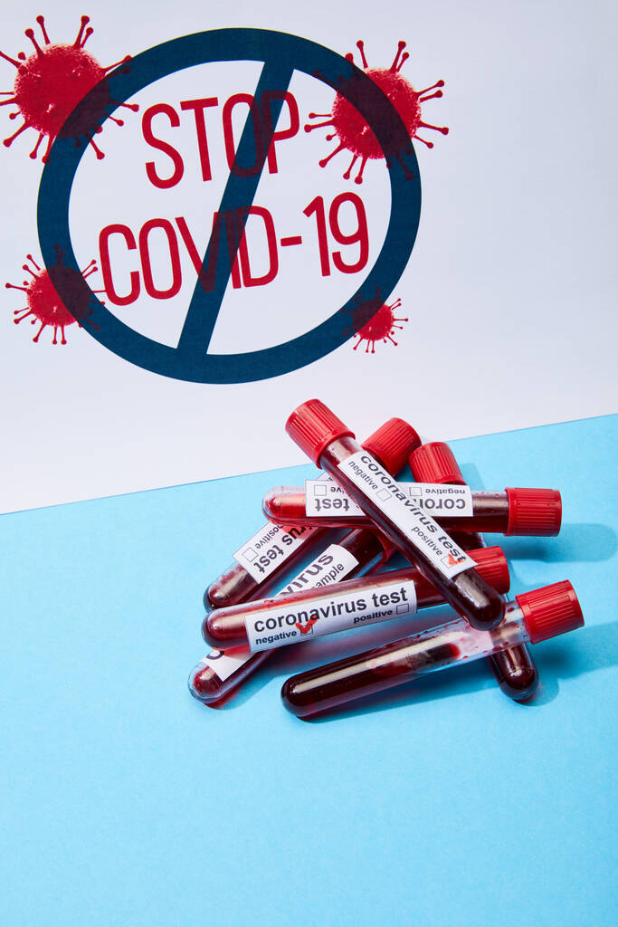 πινακίδα με γράμματα stop covid-19 κοντά σε δοκιμαστικούς σωλήνες με δείγματα αίματος και γράμματα δοκιμών του κορωναϊού σε μπλε  - Φωτογραφία, εικόνα