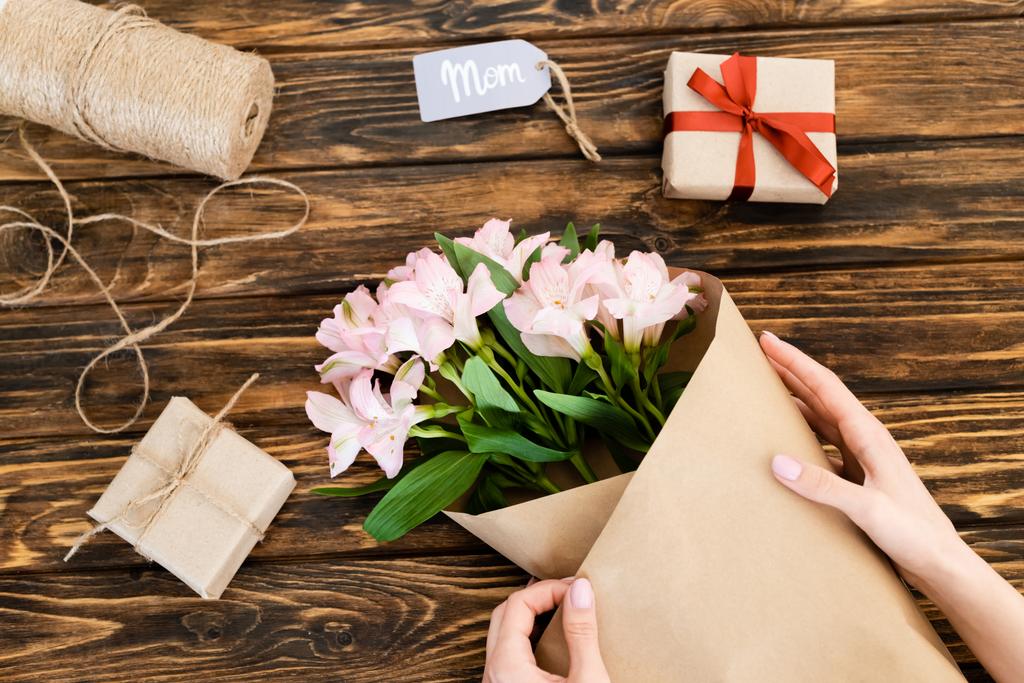 обрізаний вид жінки, що обмотує рожеві квіти в папері біля подарункових коробок на дерев'яній поверхні, концепція дня матерів
  - Фото, зображення