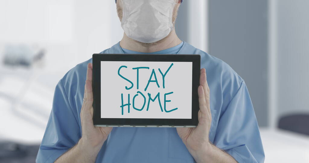 Médico con máscara facial sostiene tableta PC con STAY HOME texto escrito a mano. Autoaislamiento durante la inyección relacionada con el brote de la enfermedad COVID-19
 - Foto, Imagen