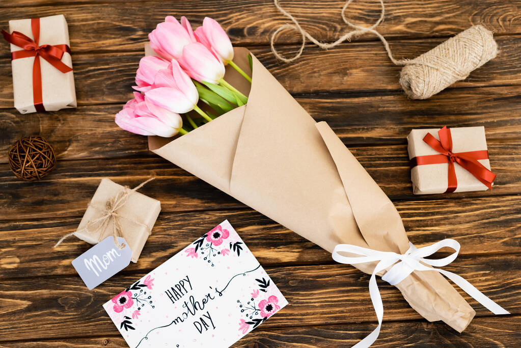 Mutlu anneler gününün olduğu tebrik kartının en üst görüntüsü hediyeler ve tahta yüzeyde çiçekler. - Fotoğraf, Görsel