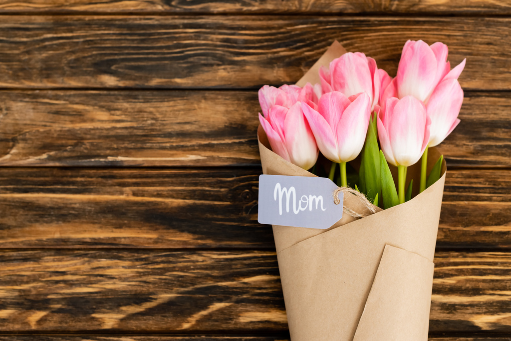vista superior de la etiqueta con letras de mamá en tulipanes rosados envueltos en papel sobre la superficie de madera, concepto de día de las madres
  - Foto, Imagen