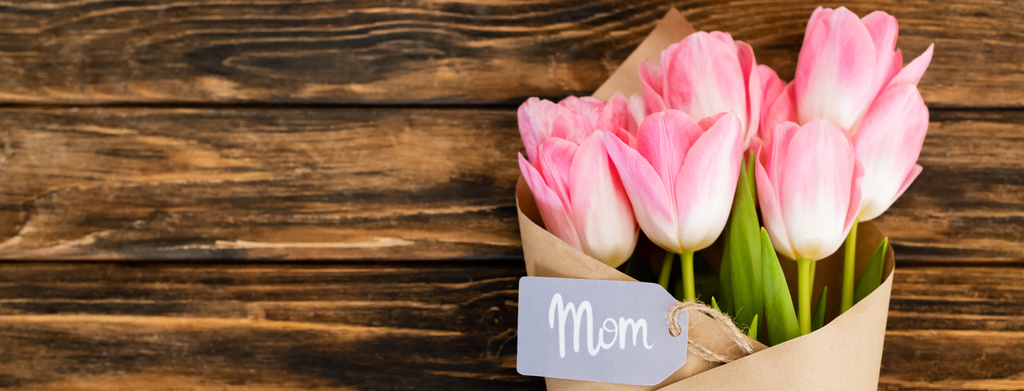 panoramic shot of tag with mom lettering on pink tulips wrapped in paper on wooden surface, mothers day concept  - Photo, Image