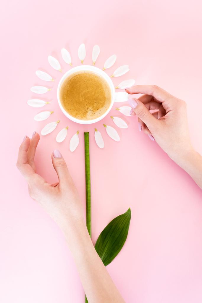 top uitzicht van de vrouw aanraken van kopje koffie in de buurt van witte bloemblaadjes op roze, moeders dag concept  - Foto, afbeelding