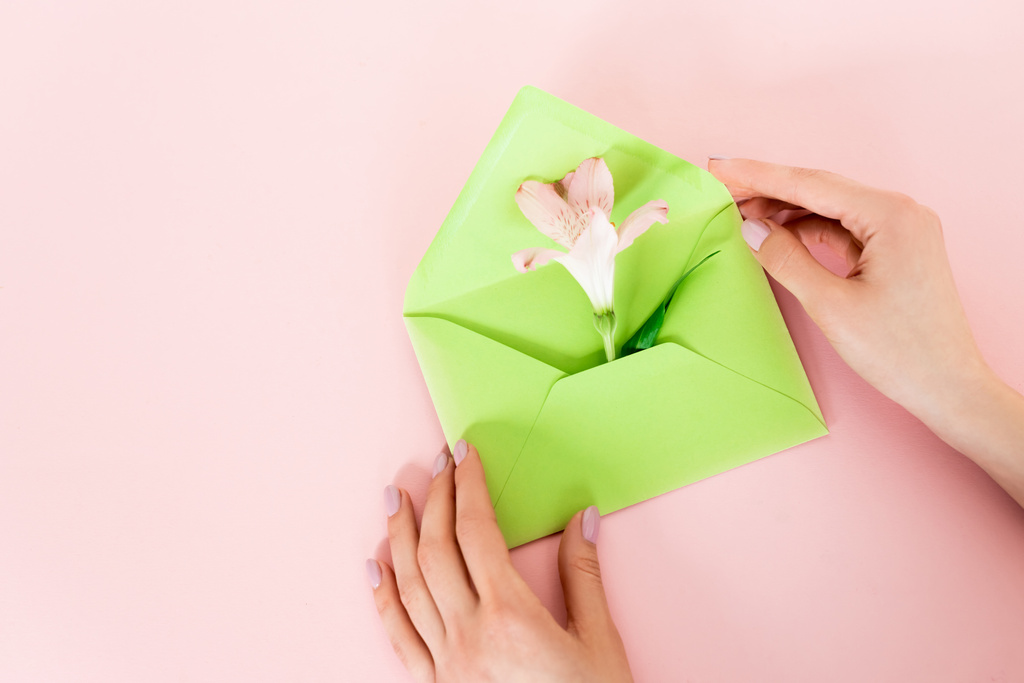 cropped view of woman holding green envelope with alstroemeria flower on pink, mothers day concept  - Photo, Image