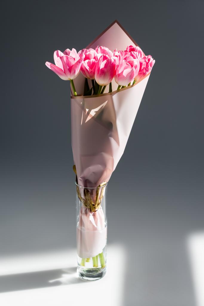 Sonnenlicht auf rosa und blühende Tulpen in der Vase mit Wasser auf grau, Muttertagskonzept - Foto, Bild