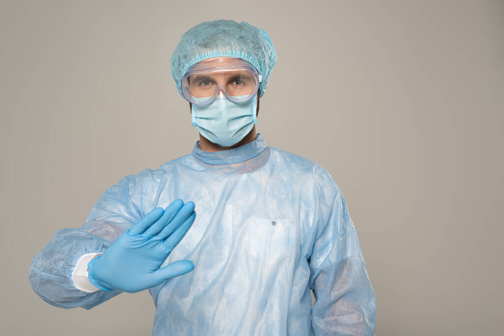Dokter in medisch masker toont stop gebaar op camera geïsoleerd op grijs - Foto, afbeelding