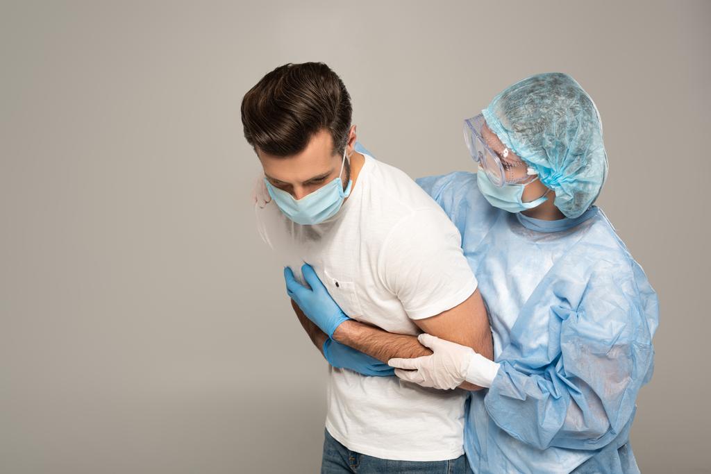 Médico abrazando paciente en máscara médica tocando pecho aislado en gris
 - Foto, Imagen