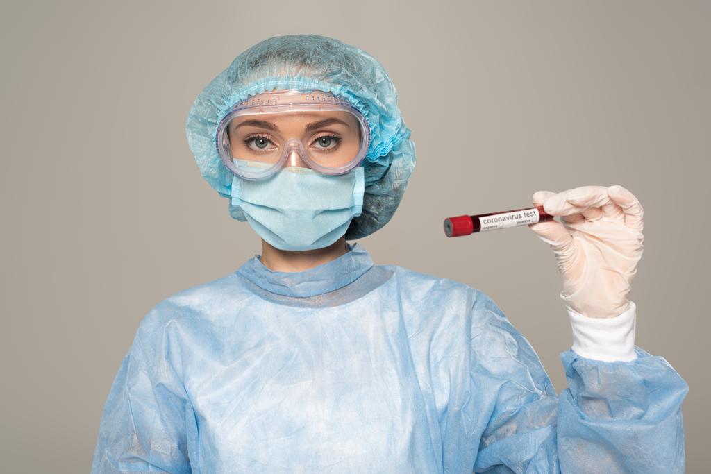 Lékař v lékařské masce a ochranné brýle držení zkumavky se vzorkem krve a koronavirem písmo izolované na šedé - Fotografie, Obrázek