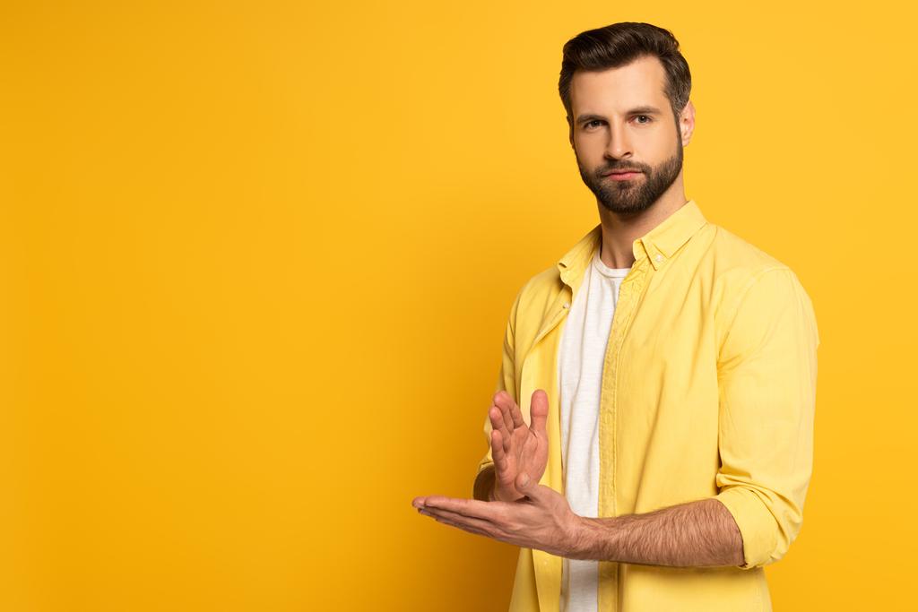 Young man looking at camera while showing gesture in deaf and dumb language on yellow background - Φωτογραφία, εικόνα