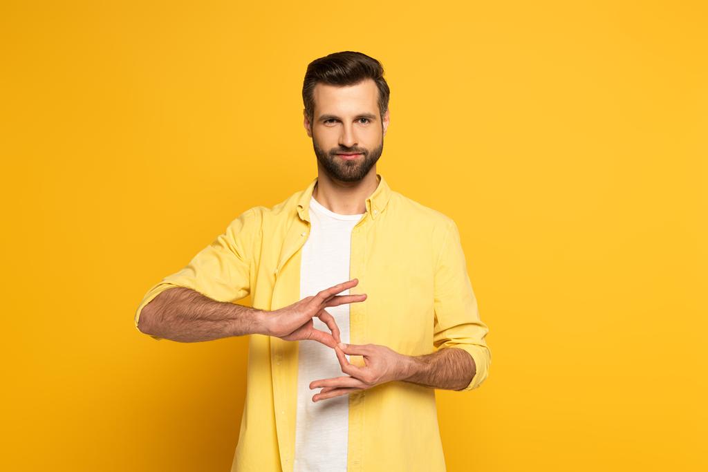 Bonito homem mostrando sinal de interpretação em linguagem surda e muda em fundo amarelo
 - Foto, Imagem