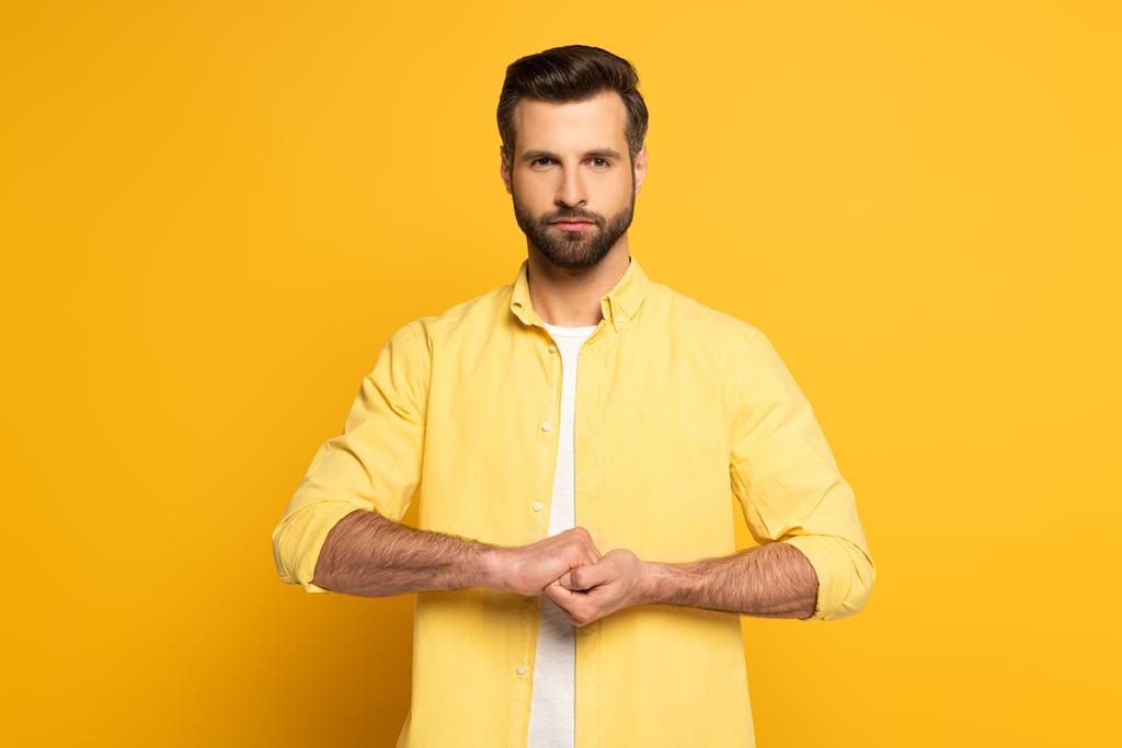 Handsome man showing cohesion sign in deaf and dumb language on yellow background - 写真・画像