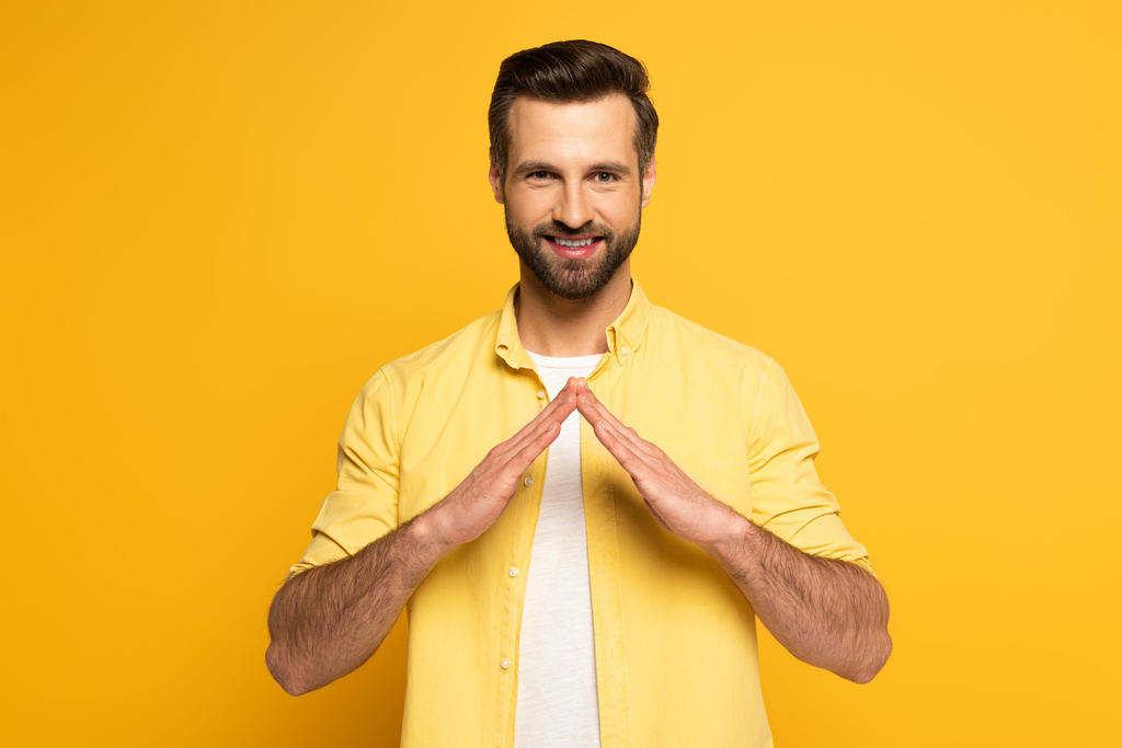 Glimlachende man toont woordhuis in gebarentaal op gele achtergrond - Foto, afbeelding