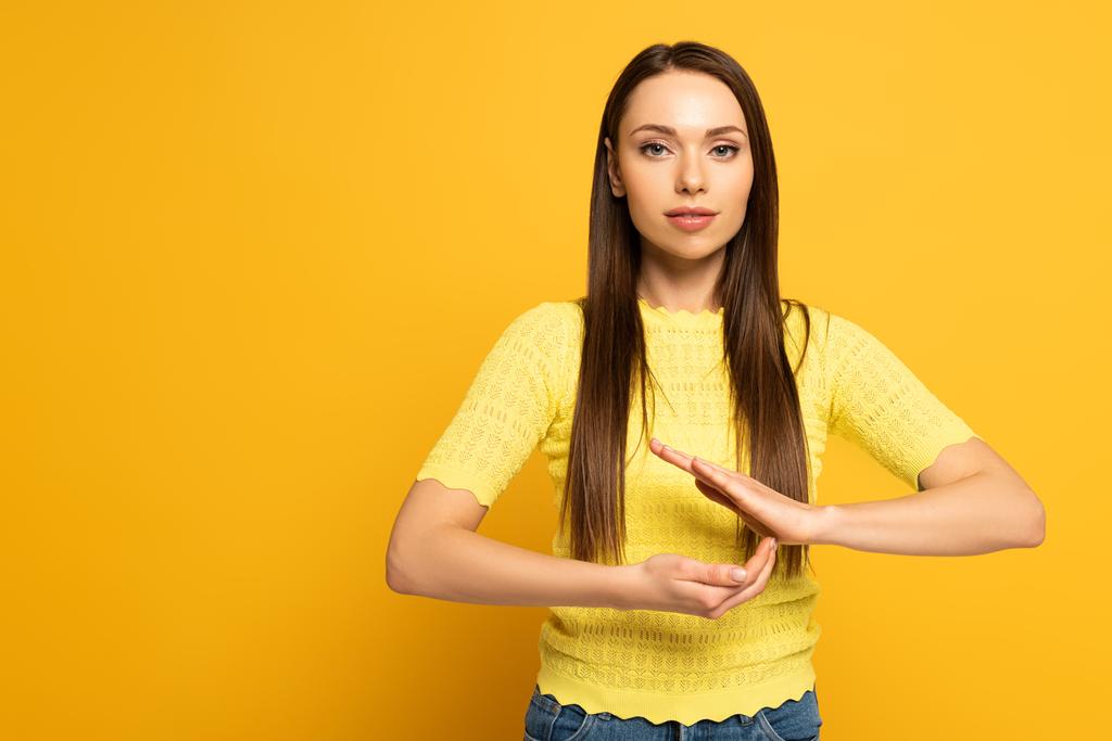 Młoda kobieta gestykuluje podczas używania języka migowego na żółtym tle - Zdjęcie, obraz