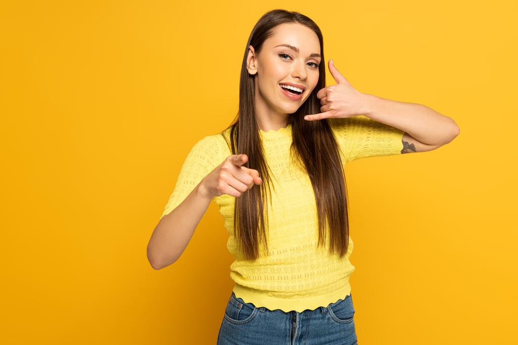 Positiivinen nainen osoittaa puhelun ele ja sormella keltaisella taustalla
 - Valokuva, kuva