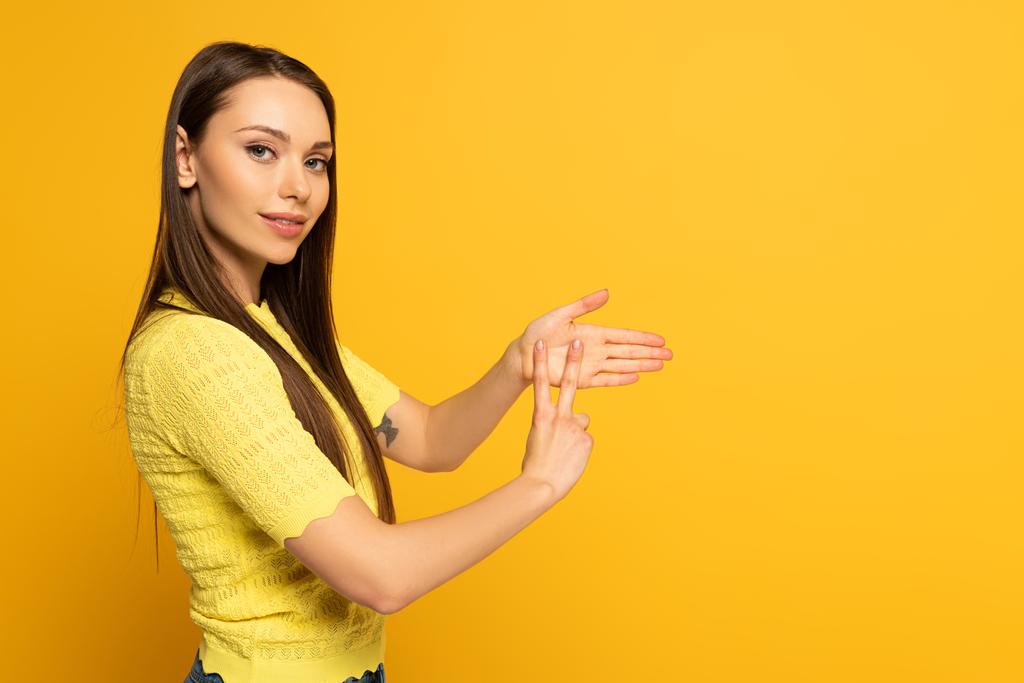 Вид сбоку женщины, показывающей жест глухим языком на желтом фоне
 - Фото, изображение