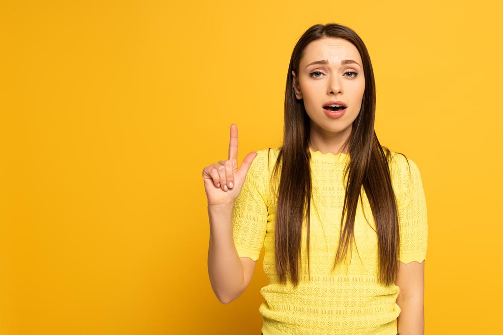 Существующая девушка показывает пальцем и смотрит на камеру на желтом фоне
 - Фото, изображение