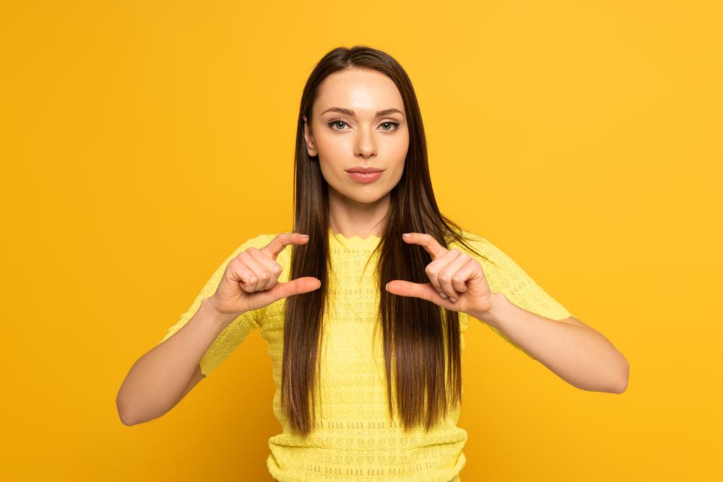 Femme regardant la caméra tout en montrant le geste du langage des signes sur fond jaune
 - Photo, image