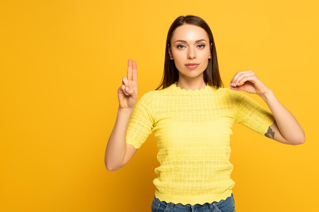 Woman showing letters in deaf and dumb language on yellow background - Zdjęcie, obraz