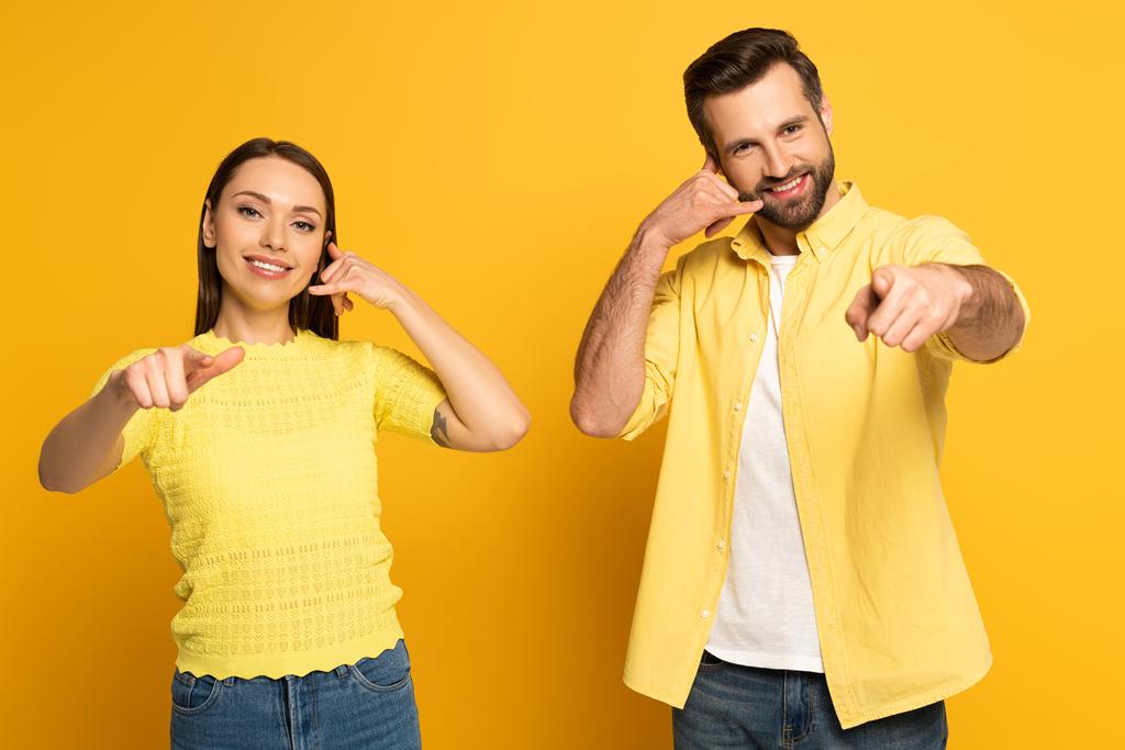 Couple positif pointant avec les doigts vers la caméra et montrant le geste d'appel sur fond jaune
 - Photo, image
