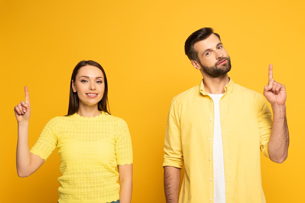Lächelndes junges Paar zeigt mit den Fingern auf gelbem Hintergrund - Foto, Bild