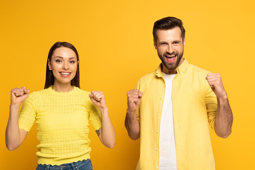 Cheerful couple showing yeah gesture at camera on yellow background - Photo, Image