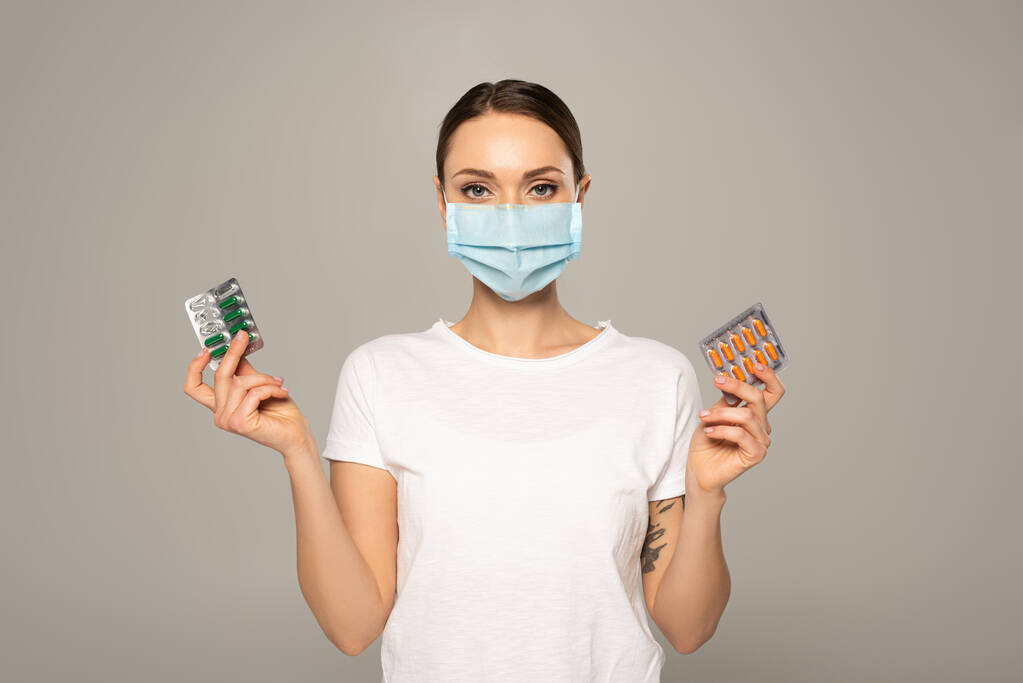 Nő orvosi maszkban tartja hólyagok pirulák izolált szürke  - Fotó, kép