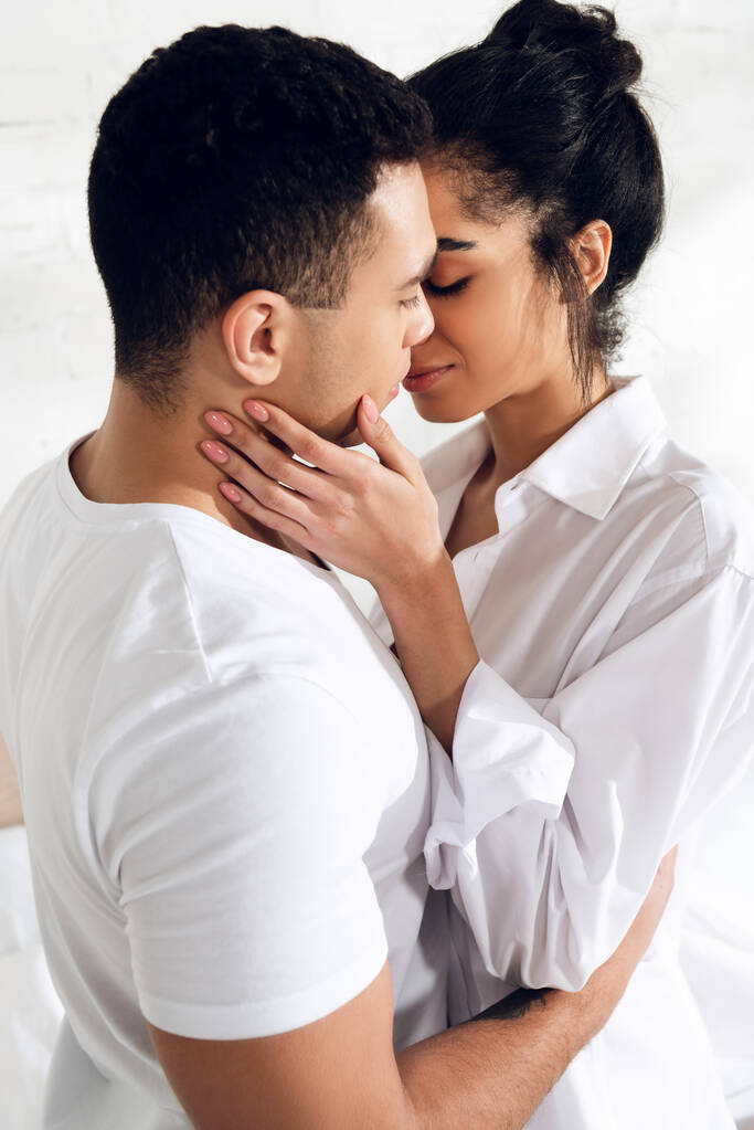 Rotujenvälinen pari halaus ja suudella suljetuin silmin makuuhuoneessa
 - Valokuva, kuva