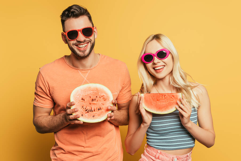 heureux jeune couple dans des lunettes de soleil montrant coupé, pastèque mûre sur fond jaune
 - Photo, image