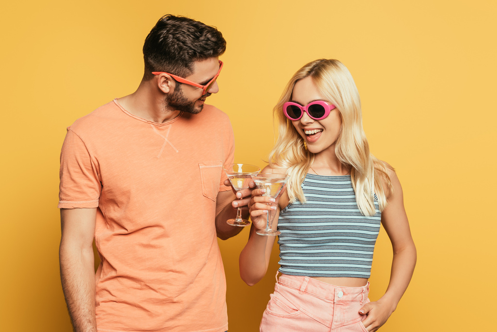 heureux jeune couple dans des lunettes de soleil cliquetis verres à cocktail sur fond jaune
 - Photo, image