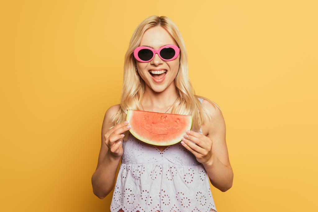 heureuse fille blonde dans des lunettes de soleil tenant tranche de pastèque sur fond jaune
 - Photo, image