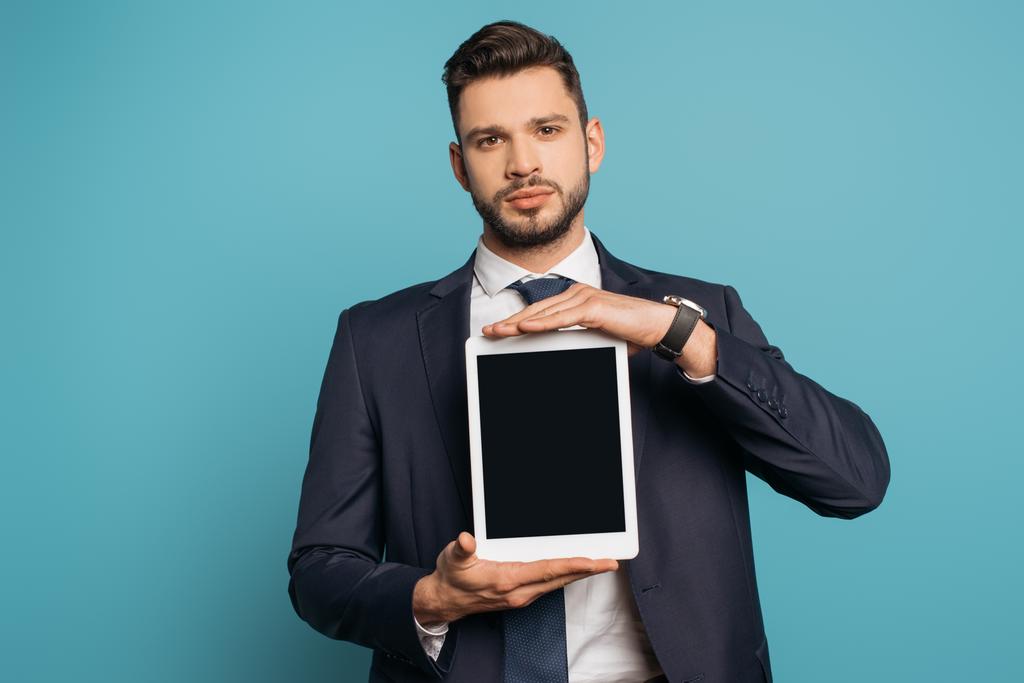 homme d'affaires confiant montrant tablette numérique avec écran vide tout en regardant la caméra sur fond bleu
 - Photo, image