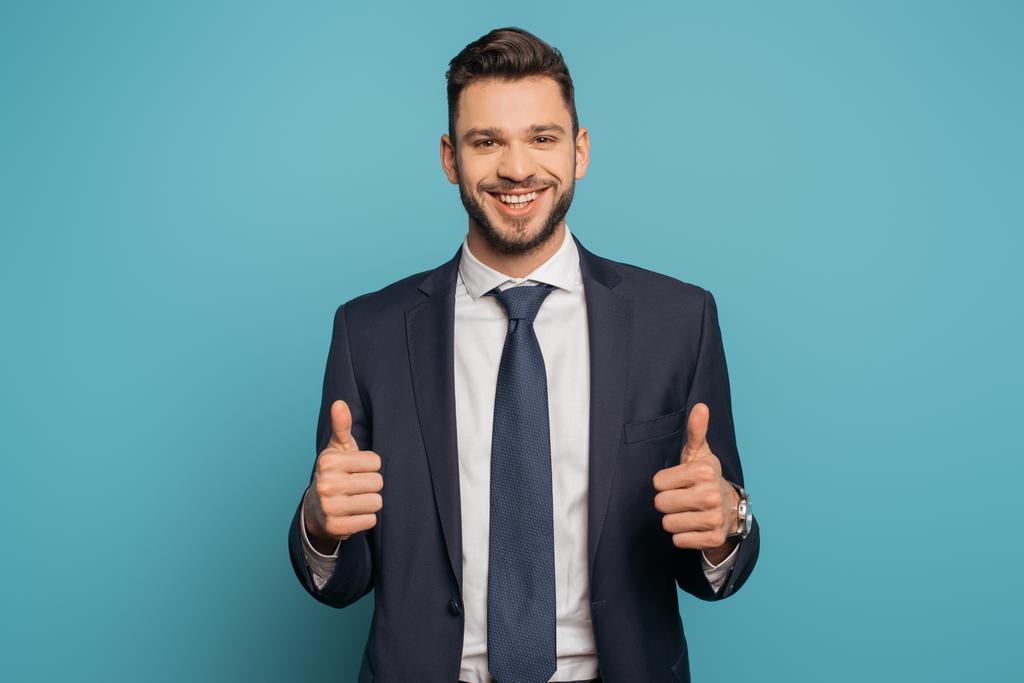 happy businessman showing thumbs up while looking at camera on blue background - Photo, Image