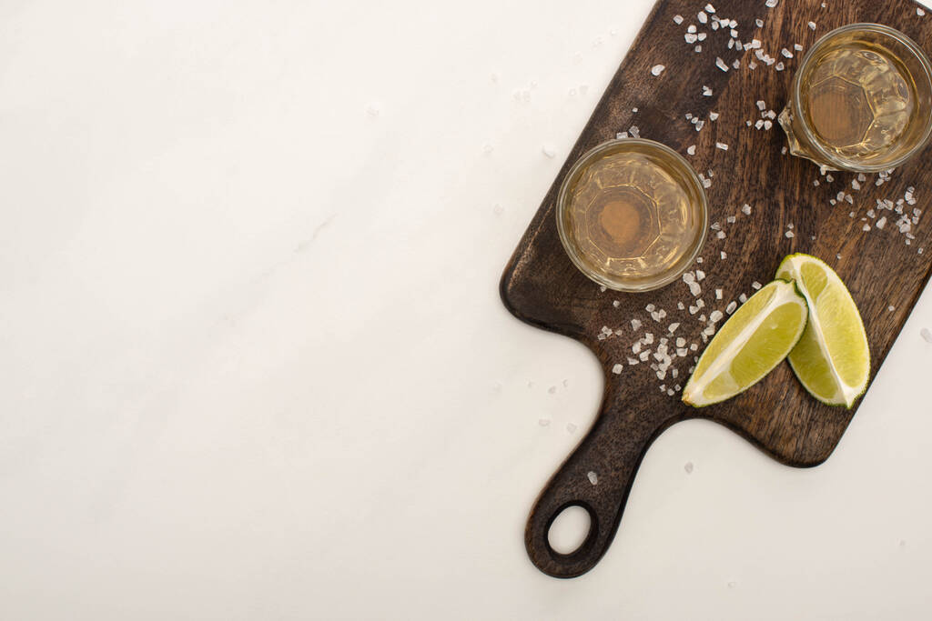 ylhäältä näkymä kultainen tequila kalkilla, suola puinen leikkuulauta valkoinen marmori pinta
 - Valokuva, kuva