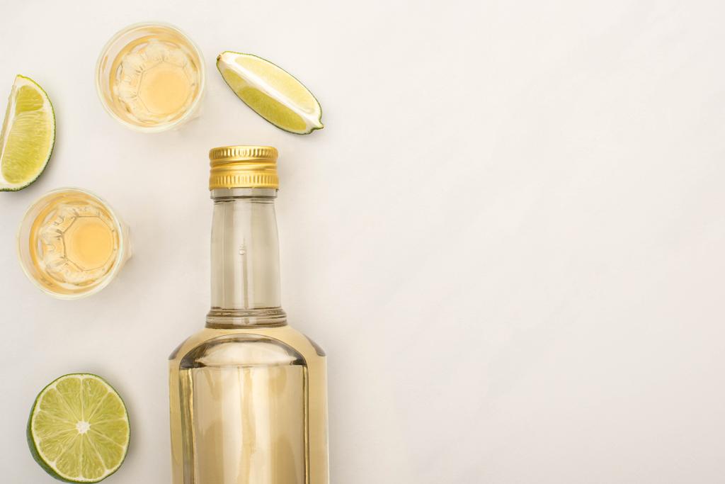 Ansicht von goldenem Tequila in Flasche und Schnapsgläsern mit Limette auf weißem Marmor - Foto, Bild
