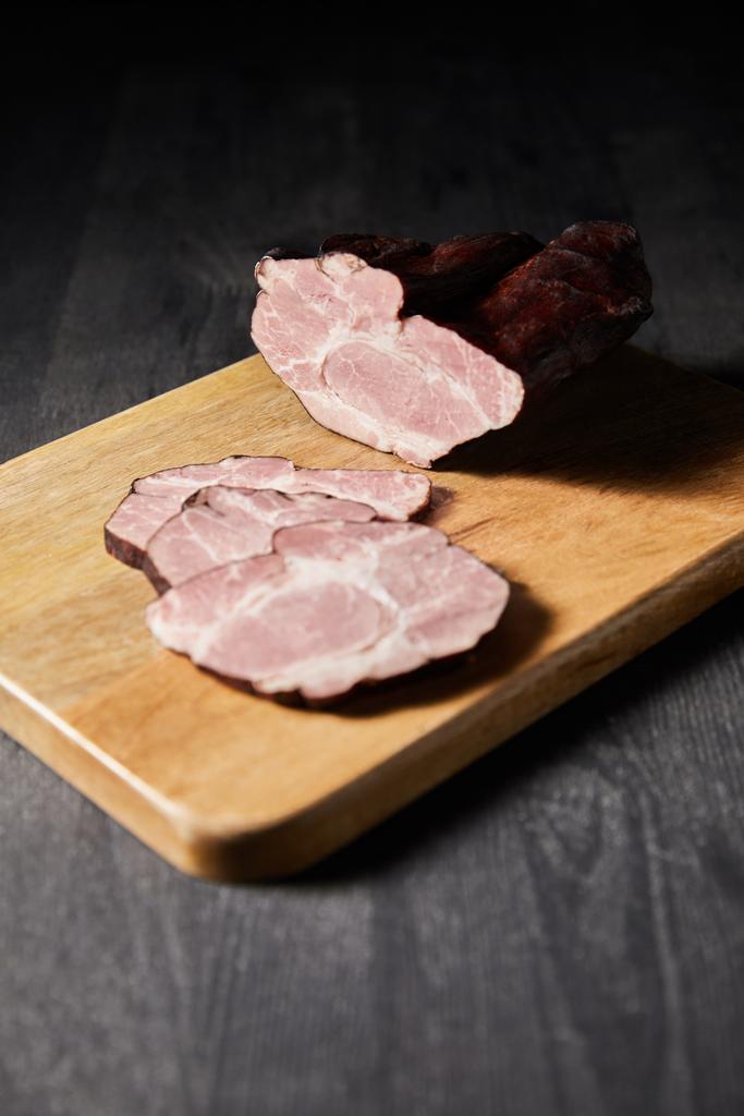 selectieve focus van smakelijke ham gesneden ham op snijplank op houten grijze tafel - Foto, afbeelding