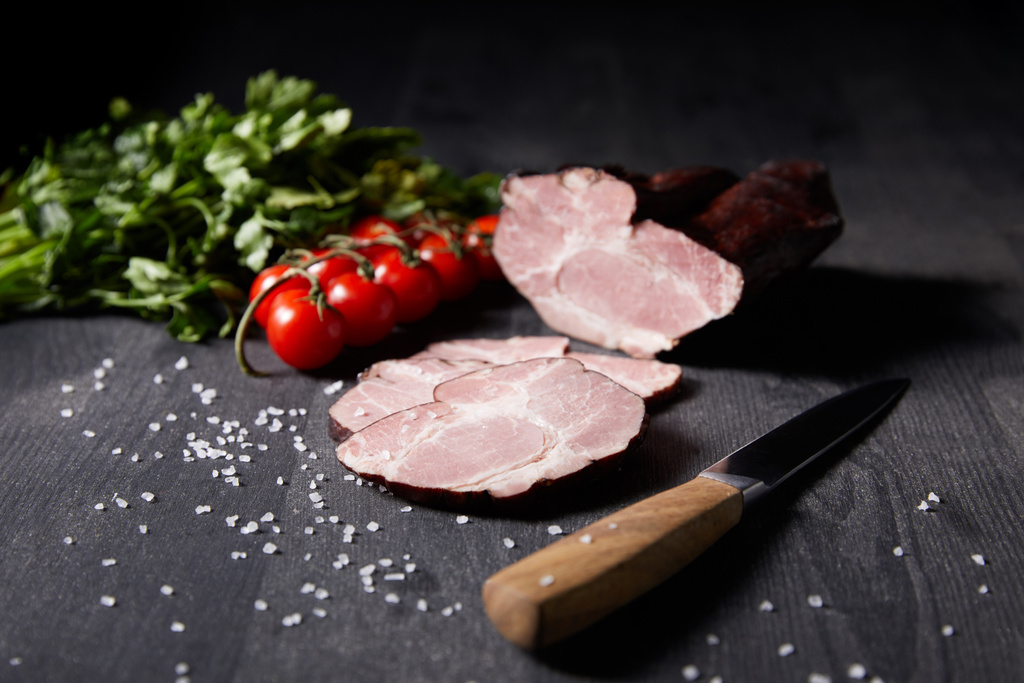 selective focus of tasty ham sliced ham, cherry tomatoes, parsley, salt, knife on wooden grey table - Photo, Image