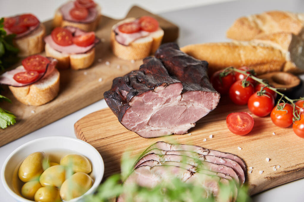 selectieve focus van smakelijke ham op snijplank met kerstomaten, olijven en stokbrood in de buurt van canape - Foto, afbeelding