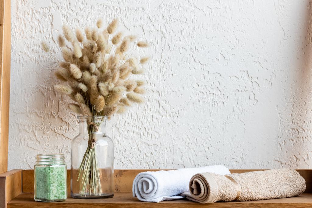 prateleira de madeira com guardanapos floridos, rolos de toalha e sal marinho verde no frasco
  - Foto, Imagem