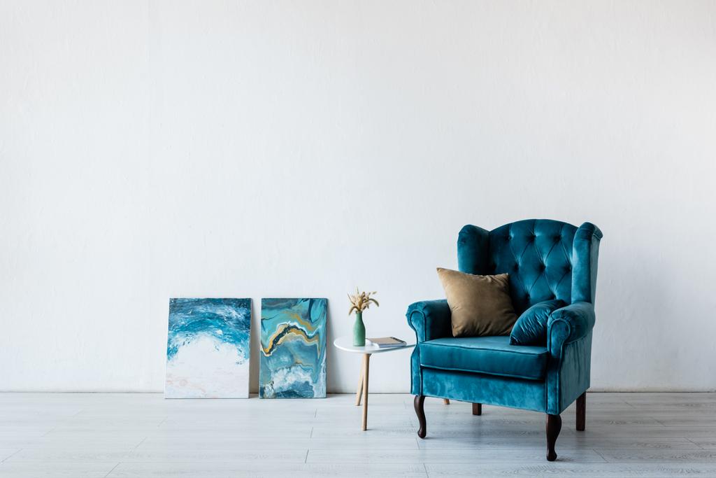 comfortable armchair near vase on coffee table and paintings in living room  - Photo, Image