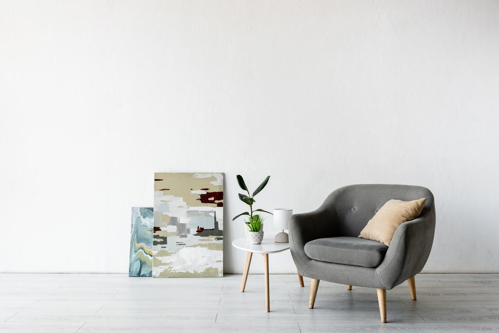 comfortabele fauteuil nabij salontafel met groene planten, lamp en schilderijen in de woonkamer  - Foto, afbeelding
