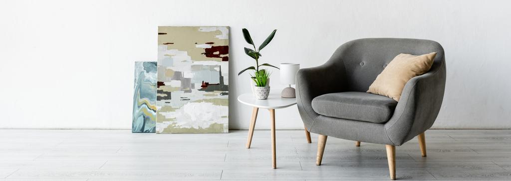 cultura panorâmica de poltrona confortável perto da mesa de café com plantas verdes, lâmpada e pinturas na sala de estar
  - Foto, Imagem