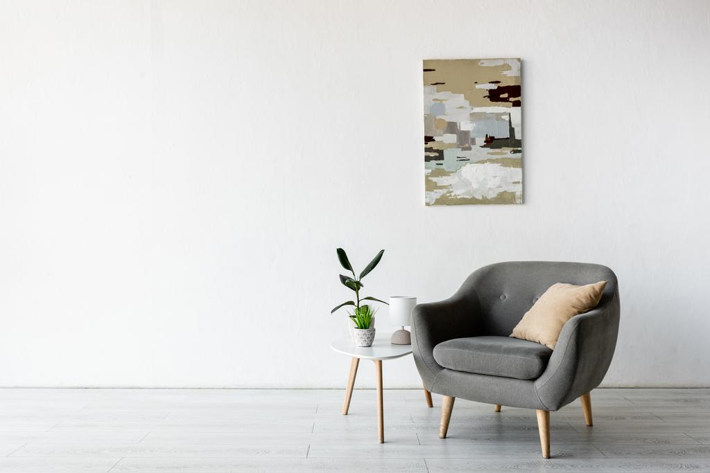 wygodny fotel przy stoliku kawowym z zielonymi roślinami, lampą i malowaniem na ścianie w salonie  - Zdjęcie, obraz